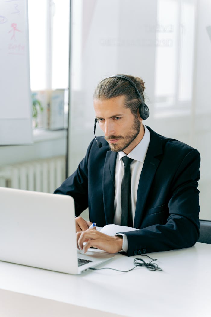 Focused customer service agent working at a desk with a headset and laptop in an office setting.
